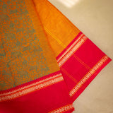 Devi Energised Cotton Saree – Golden Orange with Olive Green Floral Motifs & Vibrant Red Traditional Border